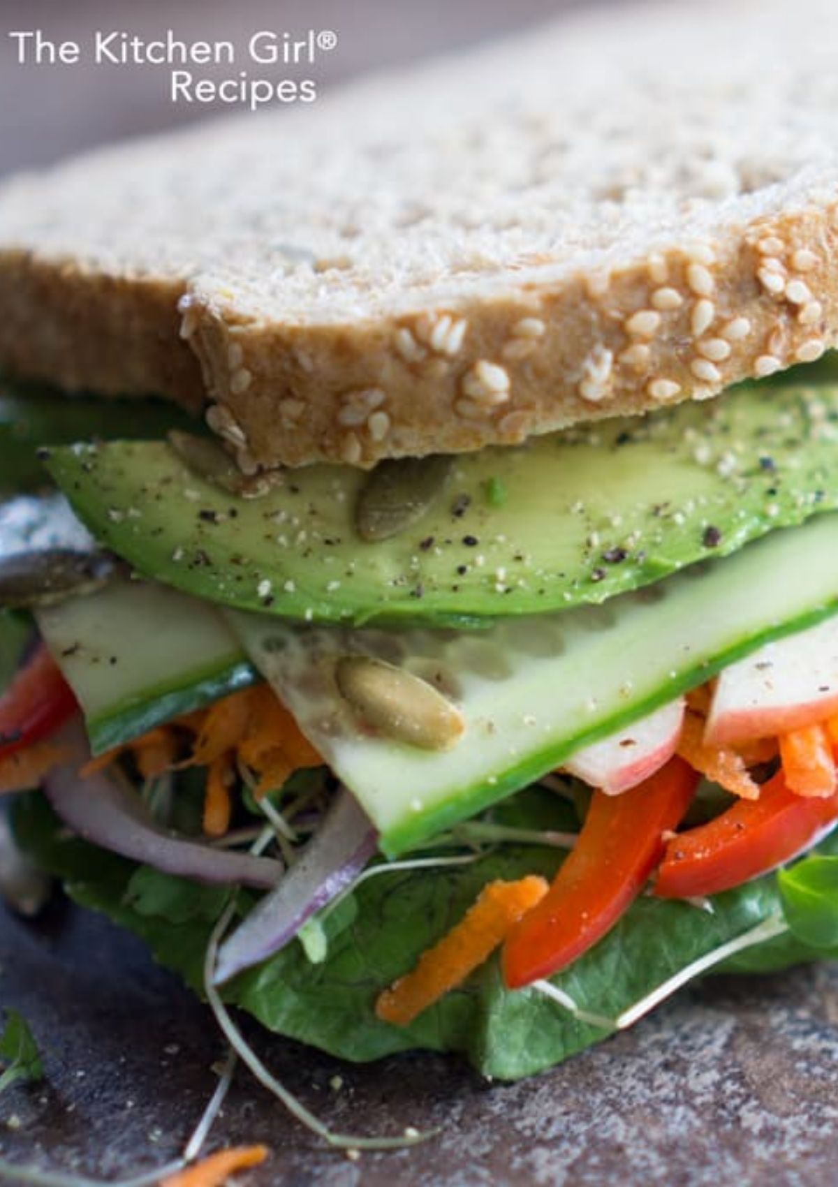 layers of vegetables like avocado, cucumber carrot, red pepper, sprouts, and greens on whole grain bread