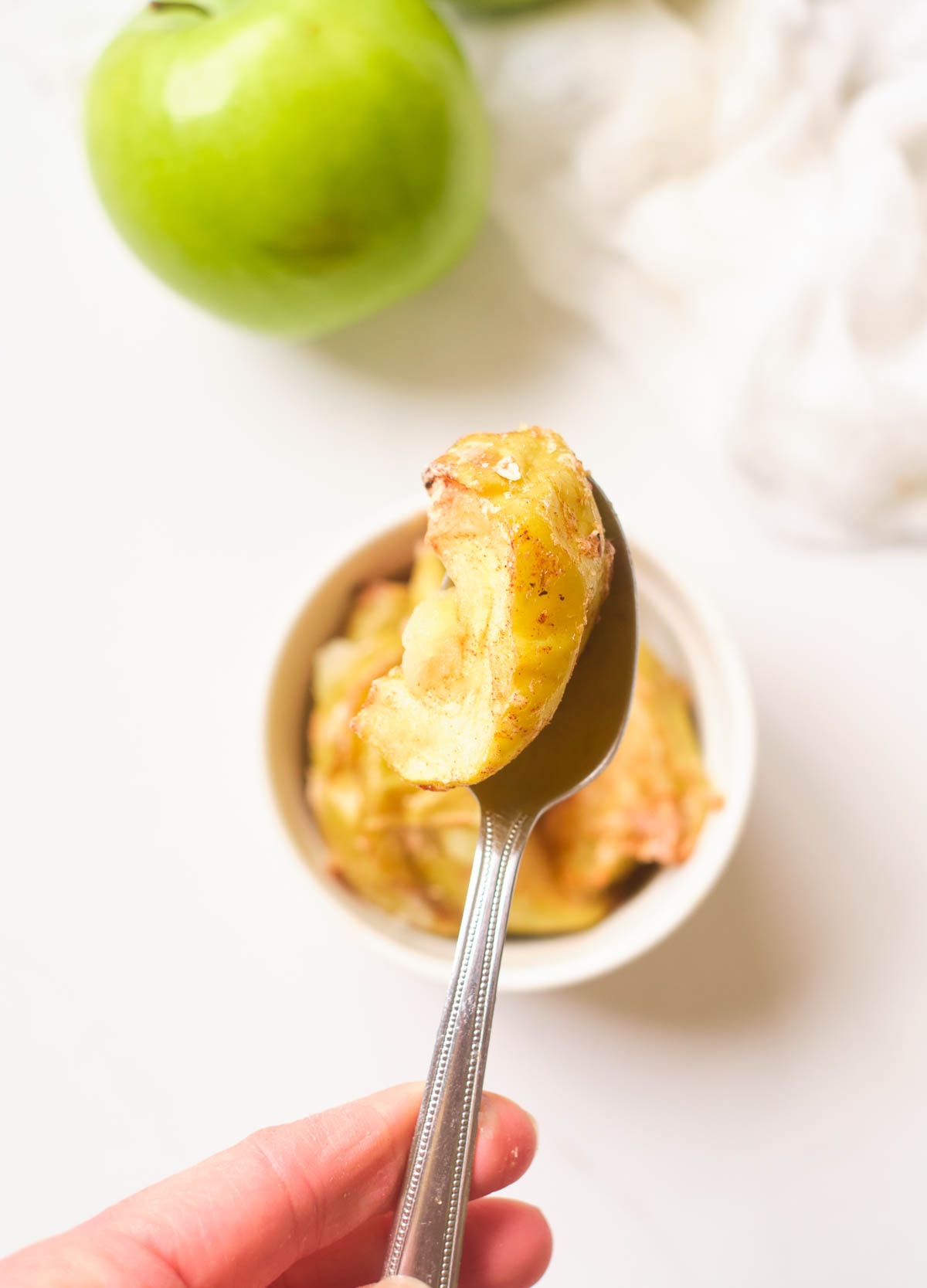 Spoon of baked air fryer apples held over ramekin filled with apple dessert.