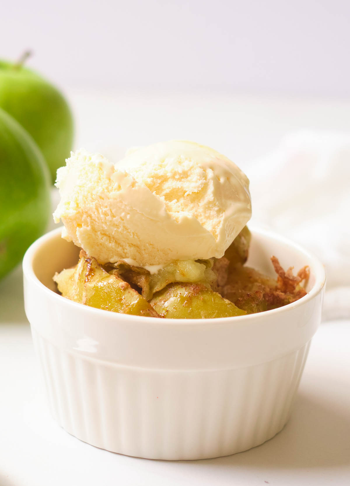 Cooked apples in small white bowl topped with ice cream. 
