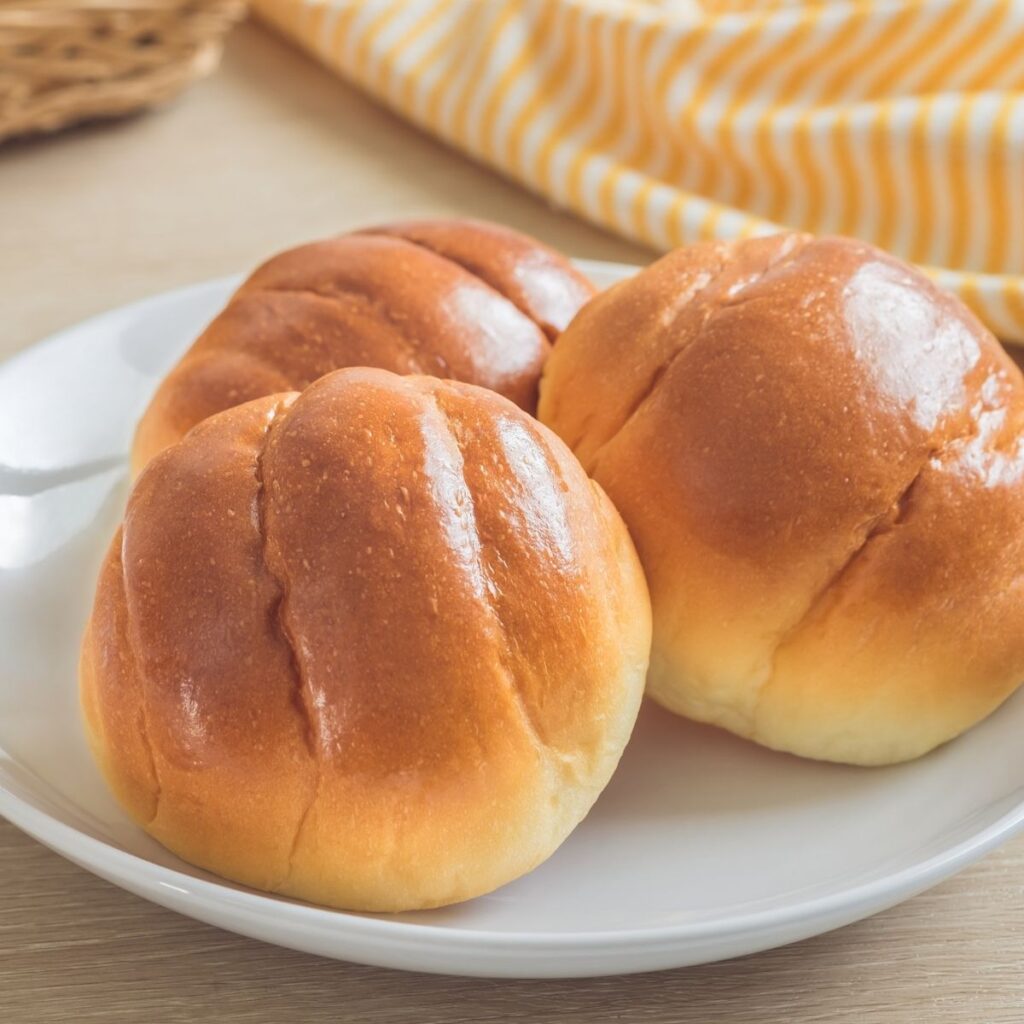 Three bread rolls on white plate.