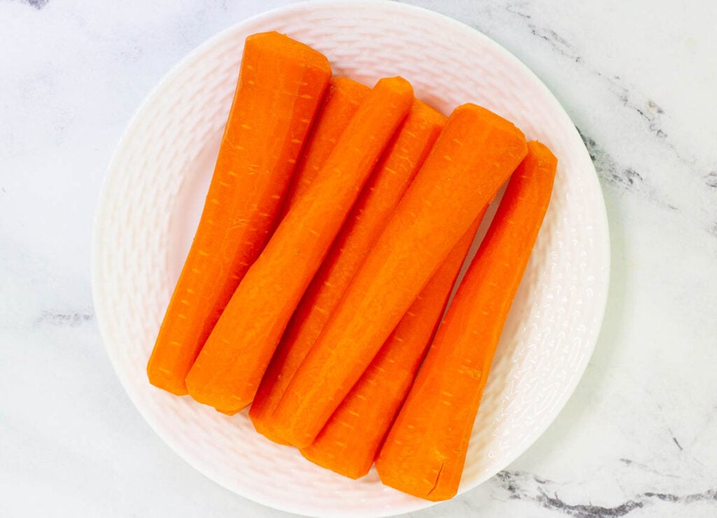Trimmed and peeled carrots on white plate.