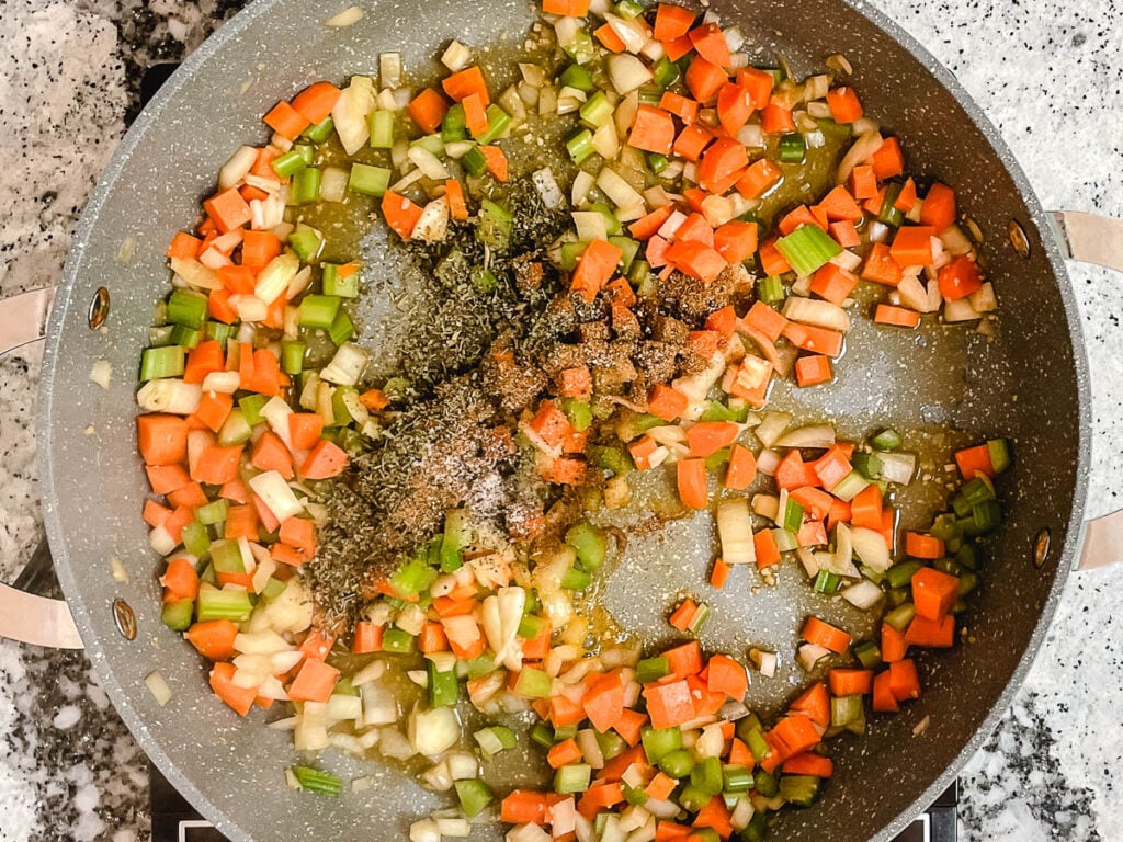 Diced vegetables in pot sprinkled with spices.