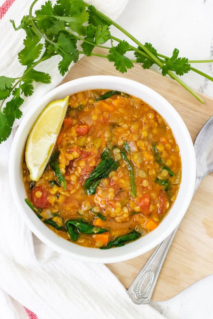 Lentil and spinach soup in white bowl with wedge of lemon.