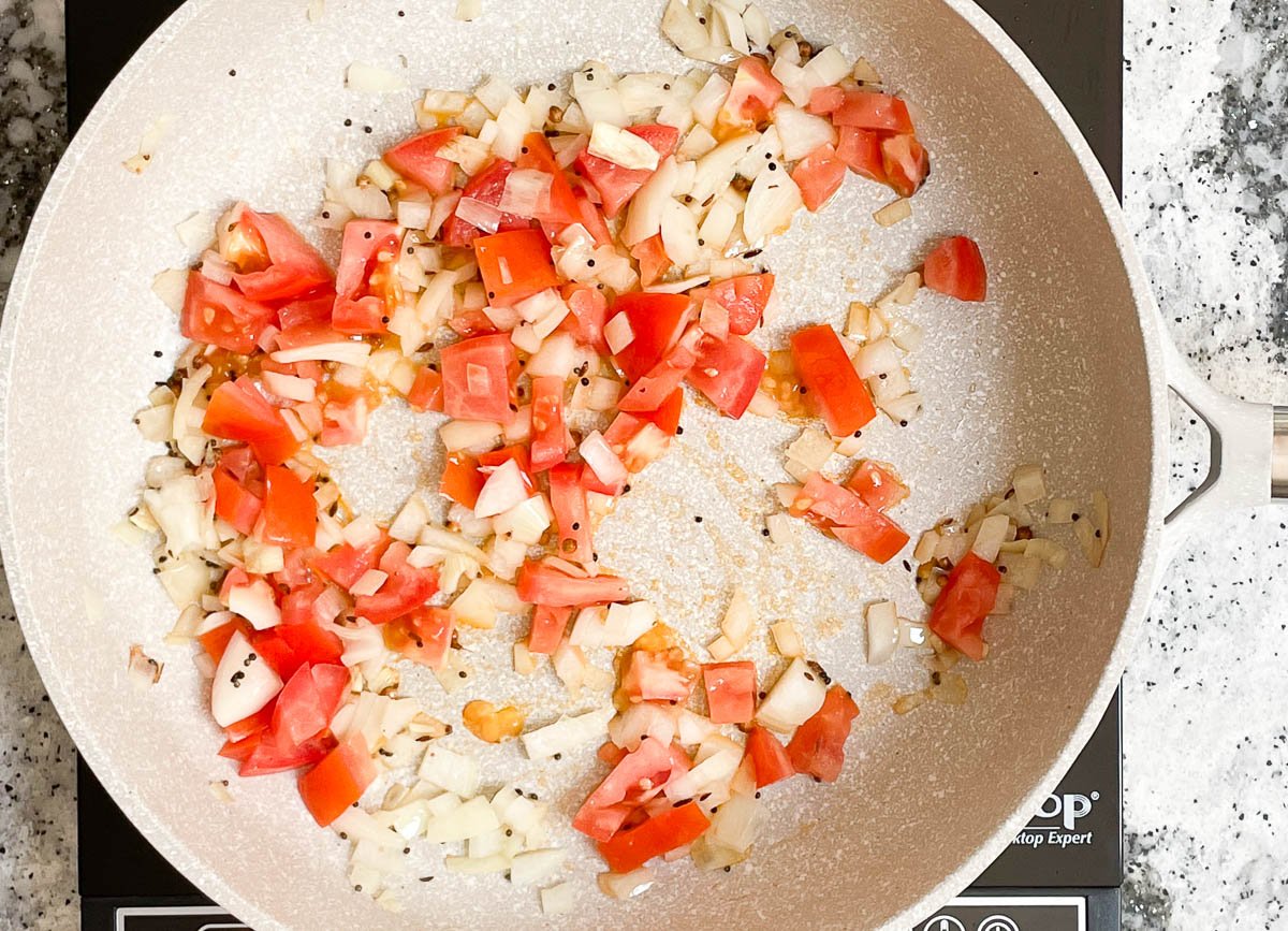 Sautédo onion, tomatoes, and spices in pot.