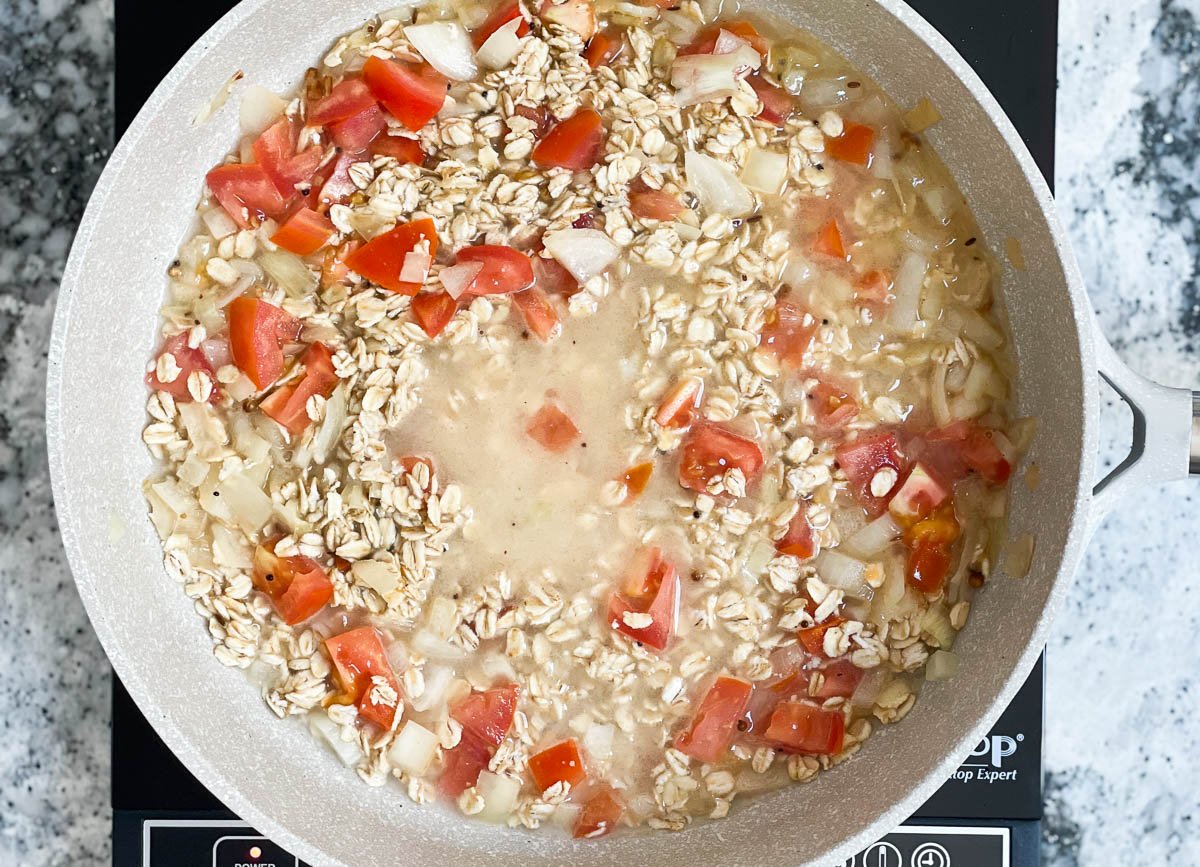Pot of oats with water, onion, and tomatoes.