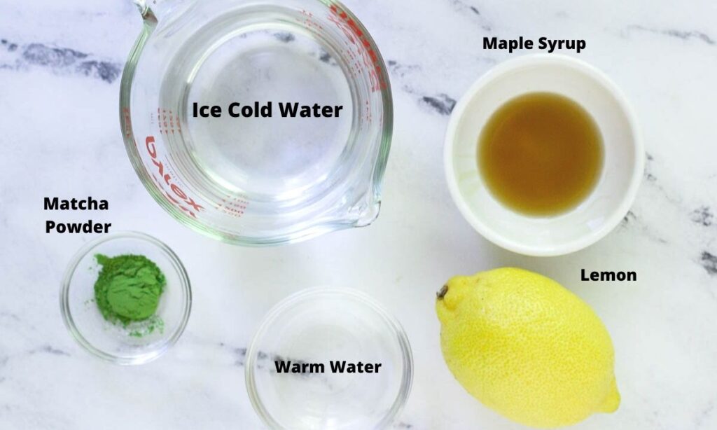 Ice cold water, maple syrup, matcha powder, lemon, and warm water on countertop.