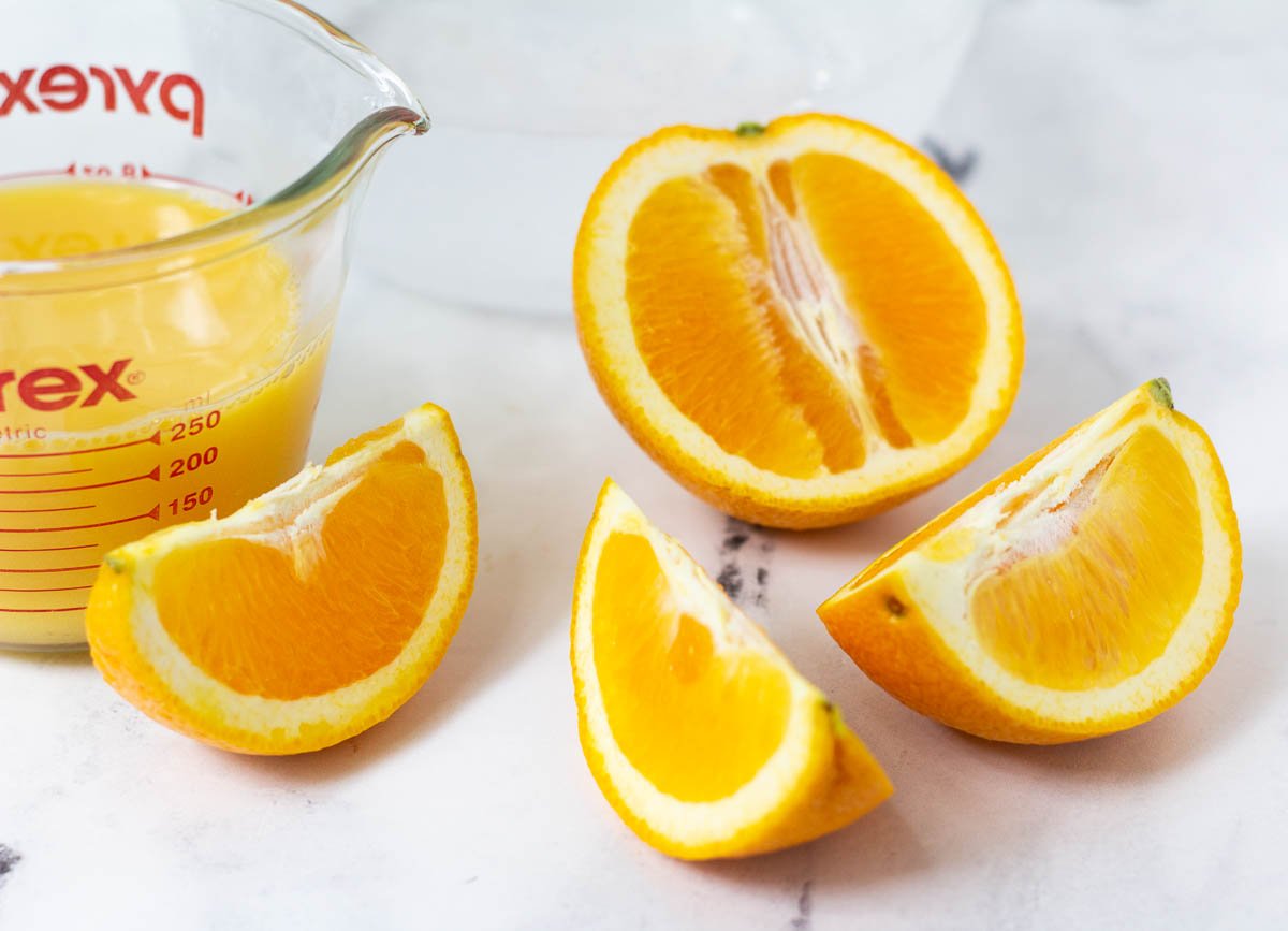 Sliced oranges beside a measuring cup filled with orange juice.