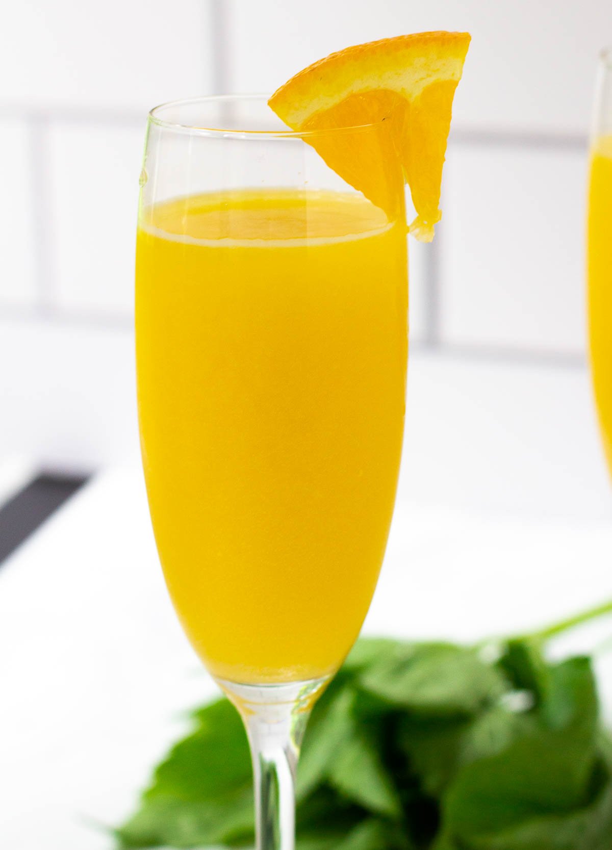 Champagne flute filled with a orange juice and sparkling water, and garnished with a wedge of orange.