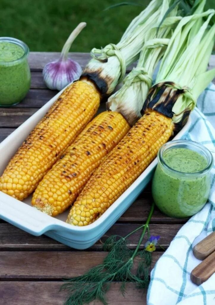 Three ears of grilled corn in ceramic dish with a side of avocado dressing.