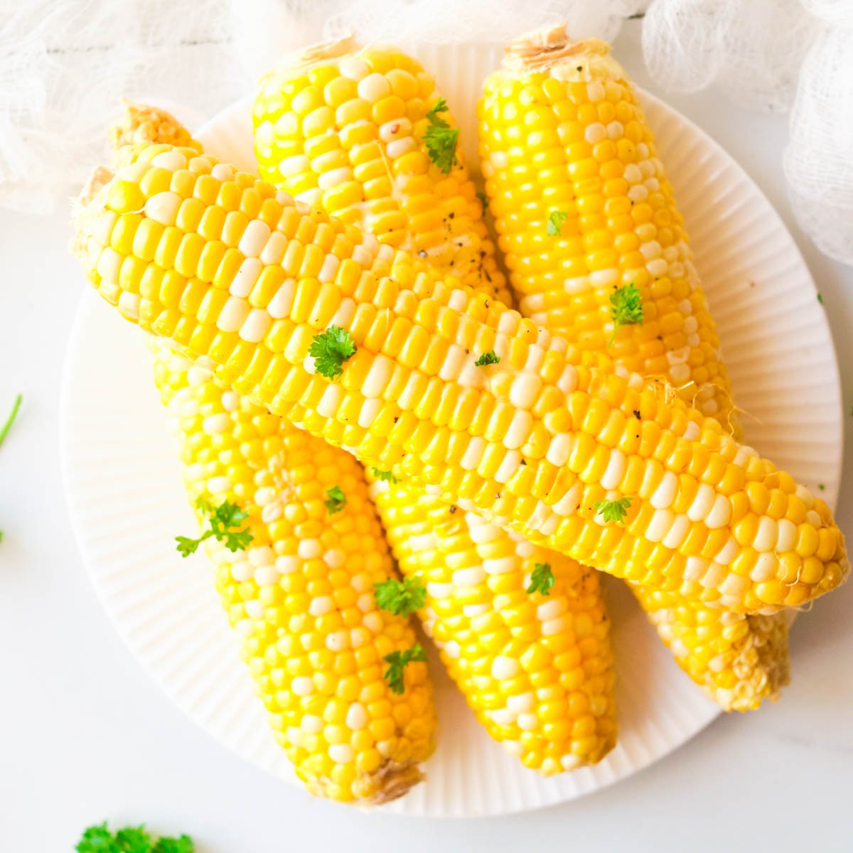 Air fryer corn on the cob stacked on plate topped with fresh parsley.