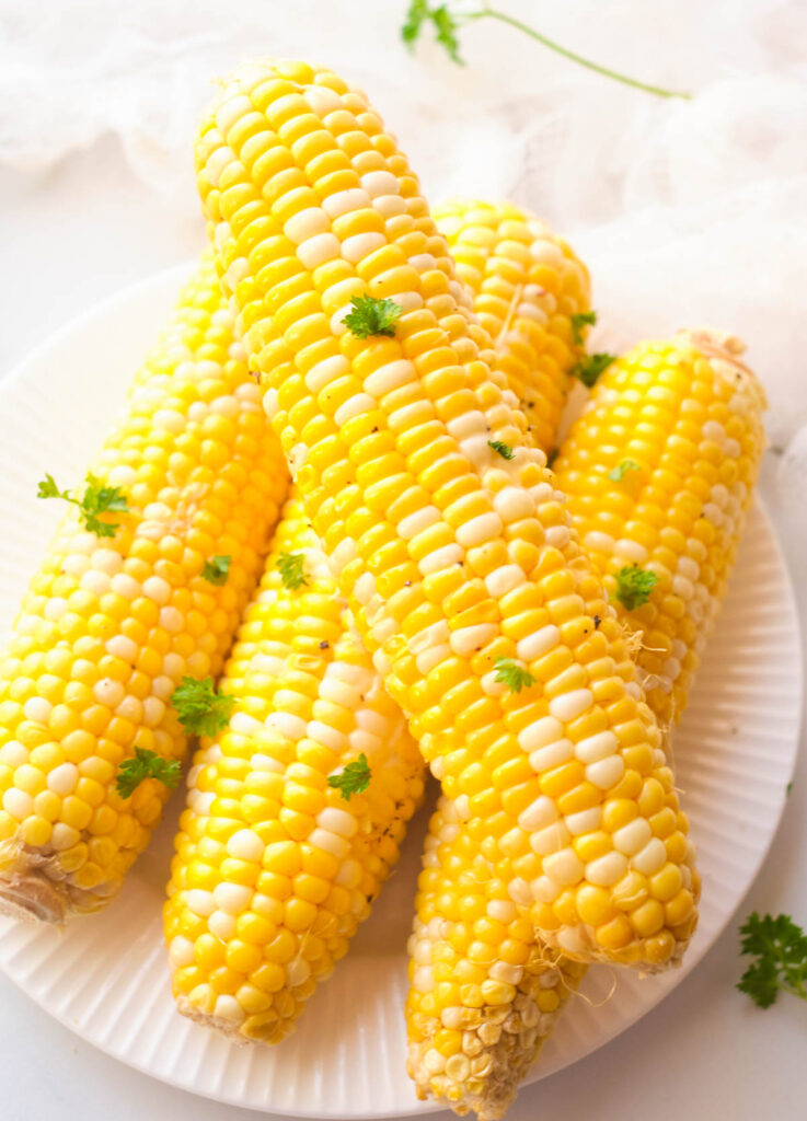 Four ears of corn topped with fresh chopped parsley.
