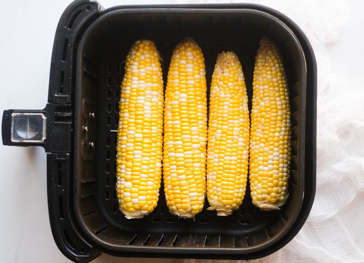 Four ears of corn in a single layer at the bottom of an air fryer basket.