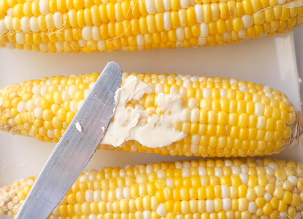 Butter knife spreading butter on cooked corn.