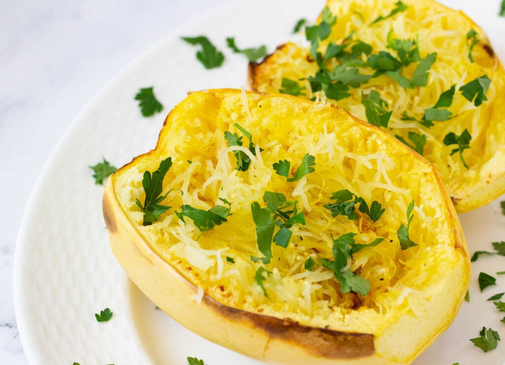 Cooked spaghetti squash halves on white platter topped with parsley.