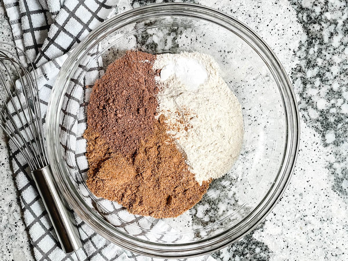 White whole wheat flour, coconut sugar, cacao powder, baking powder, baking soda, and salt in glass bowl.