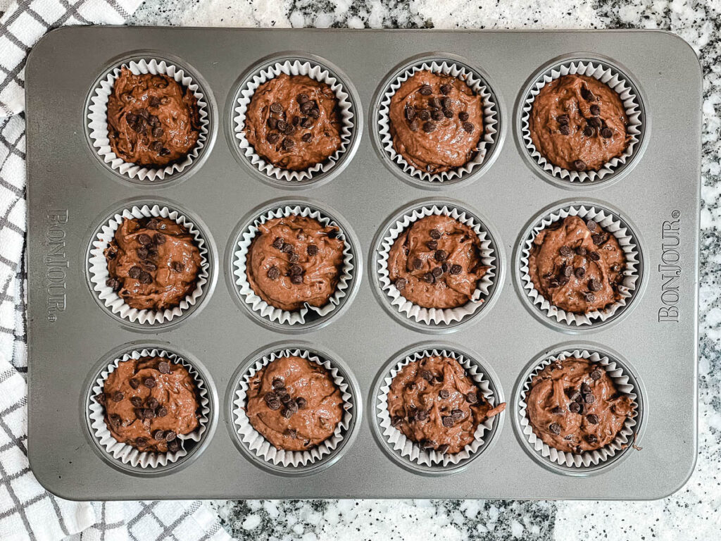 Muffin cups filled with chocolate batter and topped with chocolate chips.