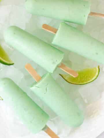 Lime popsicles on white plate with ice and lime wedges.