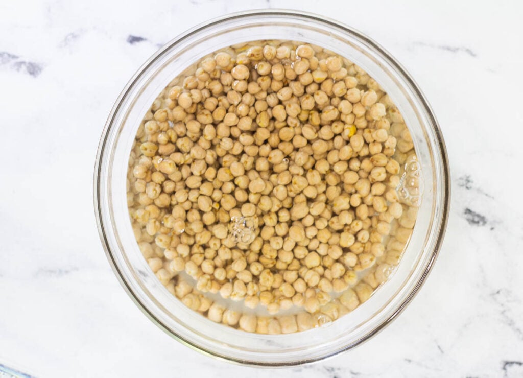 Dried chickpeas soaking in glass bowl filled with water.