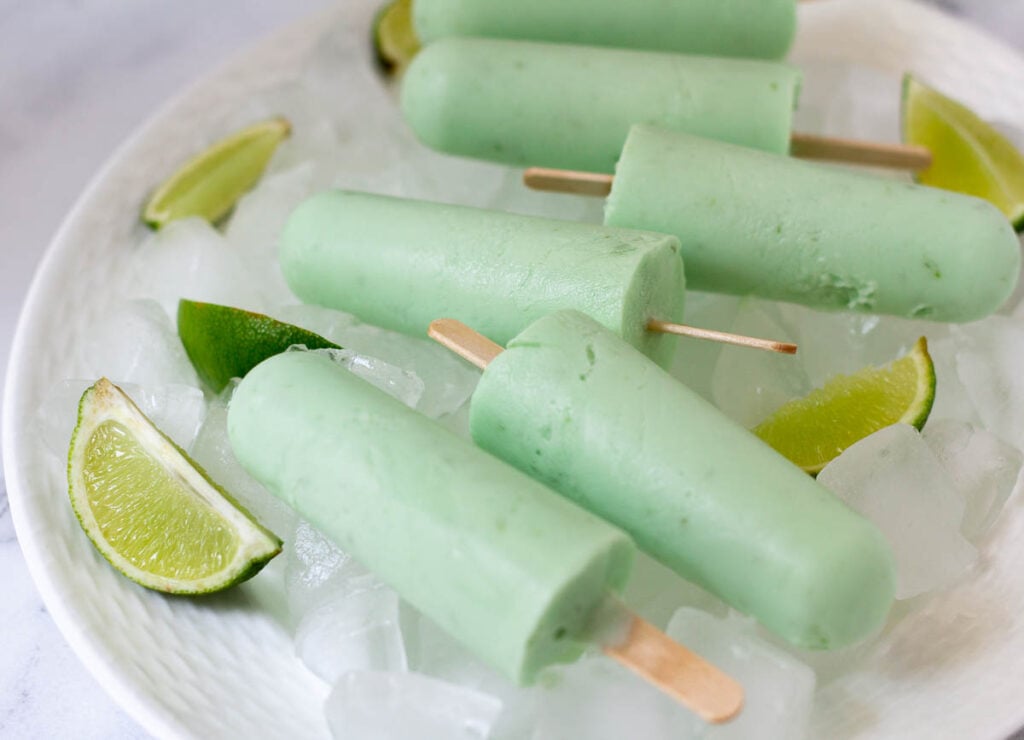 Lime popsicles on place with ice cubes and lime wedges.