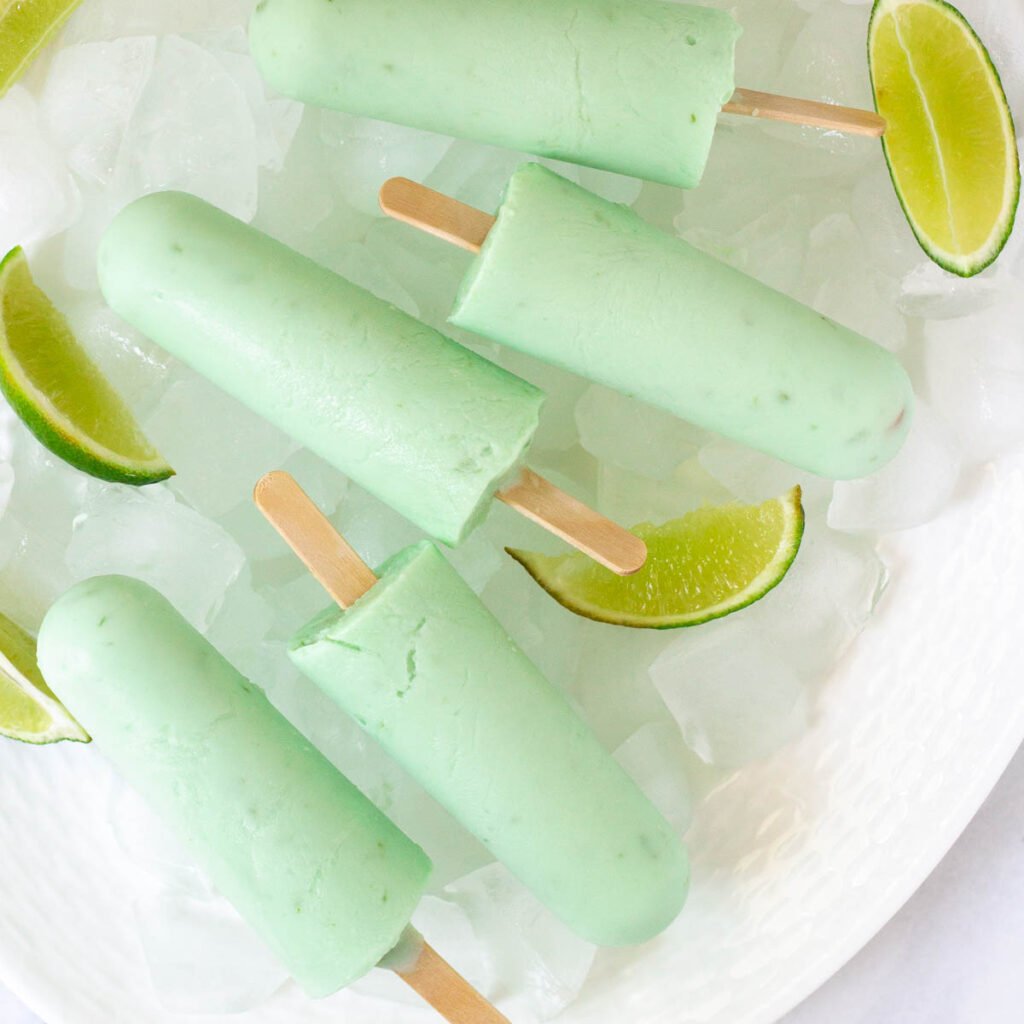 Lime popsicles on white plate with ice and lime wedges.