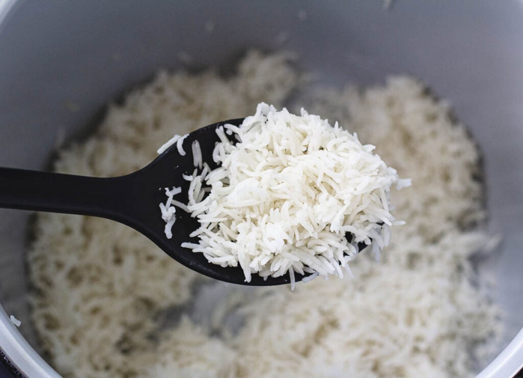 Pressure cooked white rice on black serving spoon, held above Ninja foodi bowl.