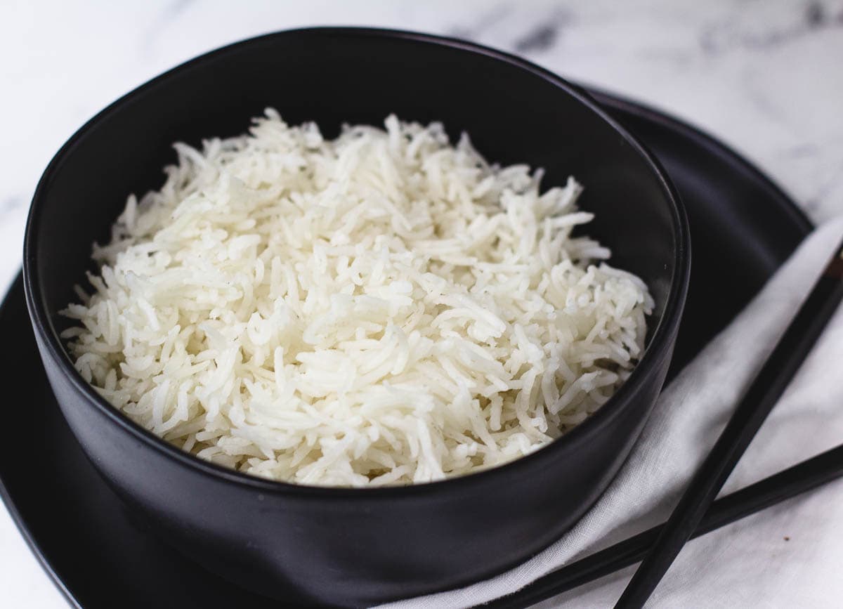 Long grain white rice in black bowl with chopsticks.