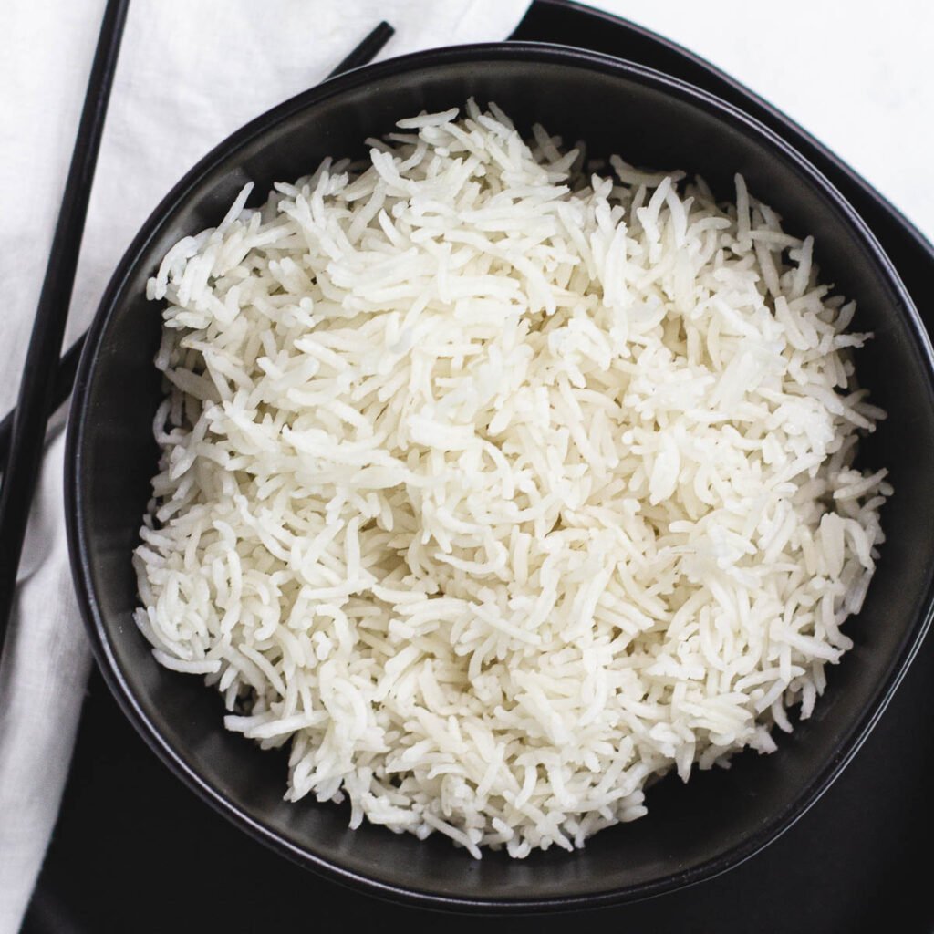 Long grain white rice in black bowl with chopsticks.