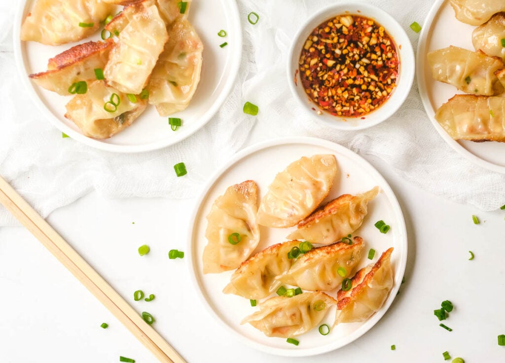 Crispy cooked dumplings on white plates, with a side of spicy garlic soy sauce.