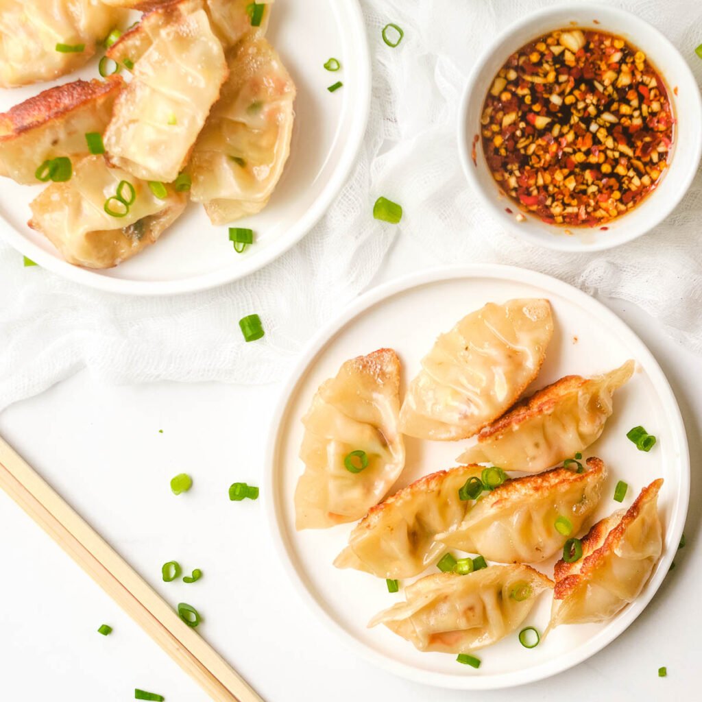 Vegan dumplings on white plate served beside dipping sauce and chopsticks.