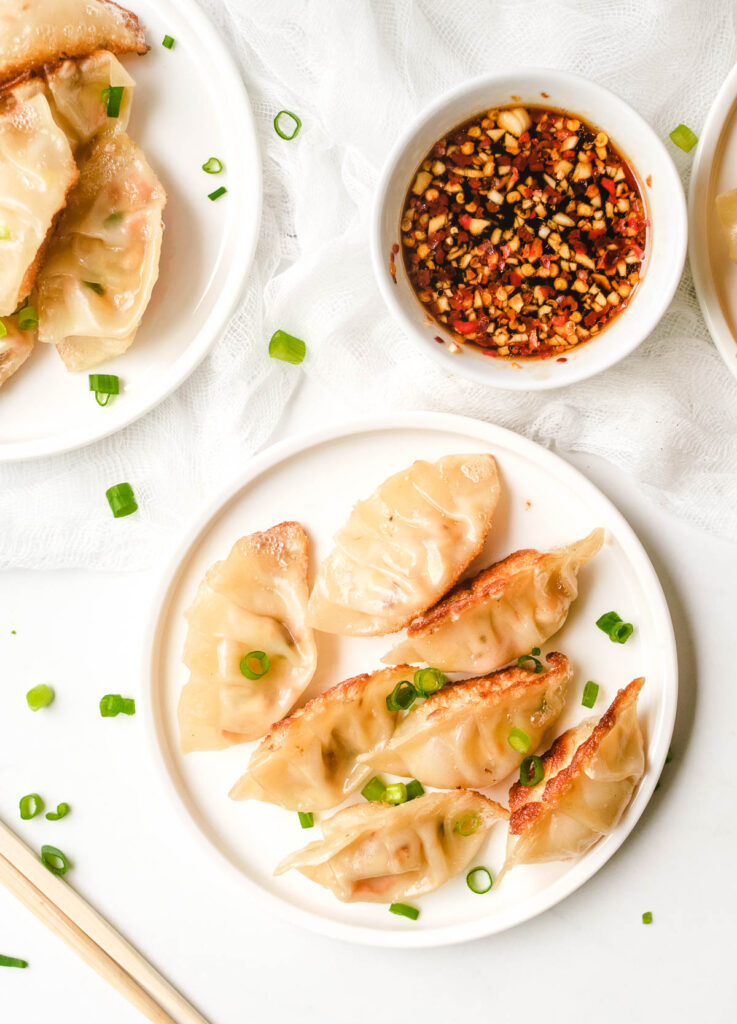 Crispy dumplings on white plate topped with scallions.