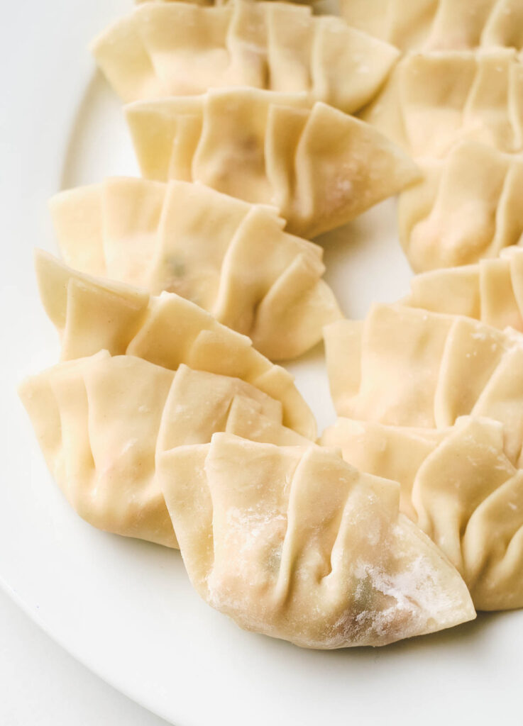 Folded, uncooked dumplings on white plate.