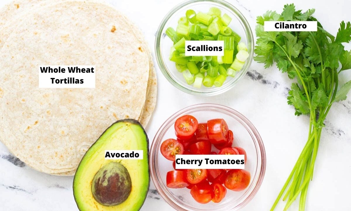 Vegan taco toppings: whole wheat tortillas, scallions, cilantro, cherry tomatoes, and avocado.