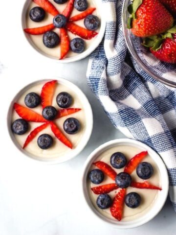 3 ramekins filled with vegan vanilla pudding and topped with strawberries and blueberries in a star pattern.
