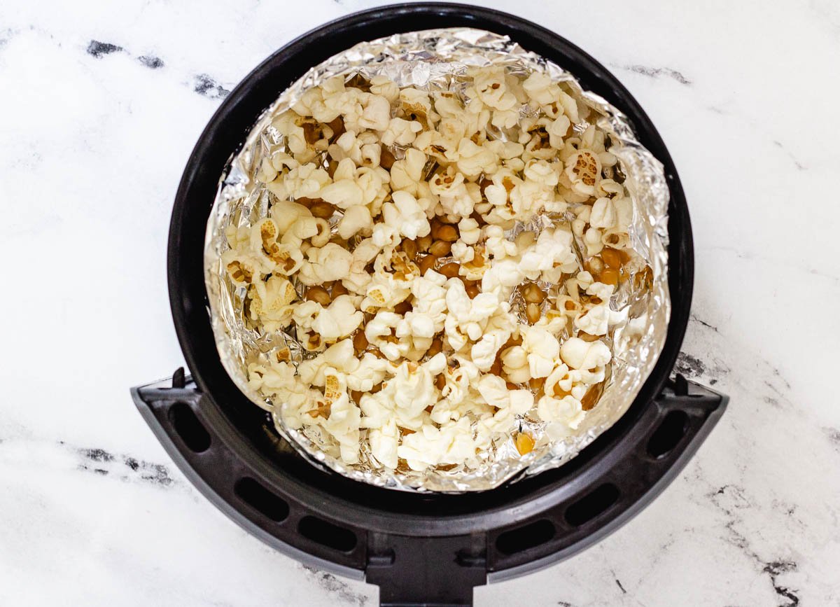 Popped and un-popped corn kernels in air fryer basket lined with aluminum foil. 