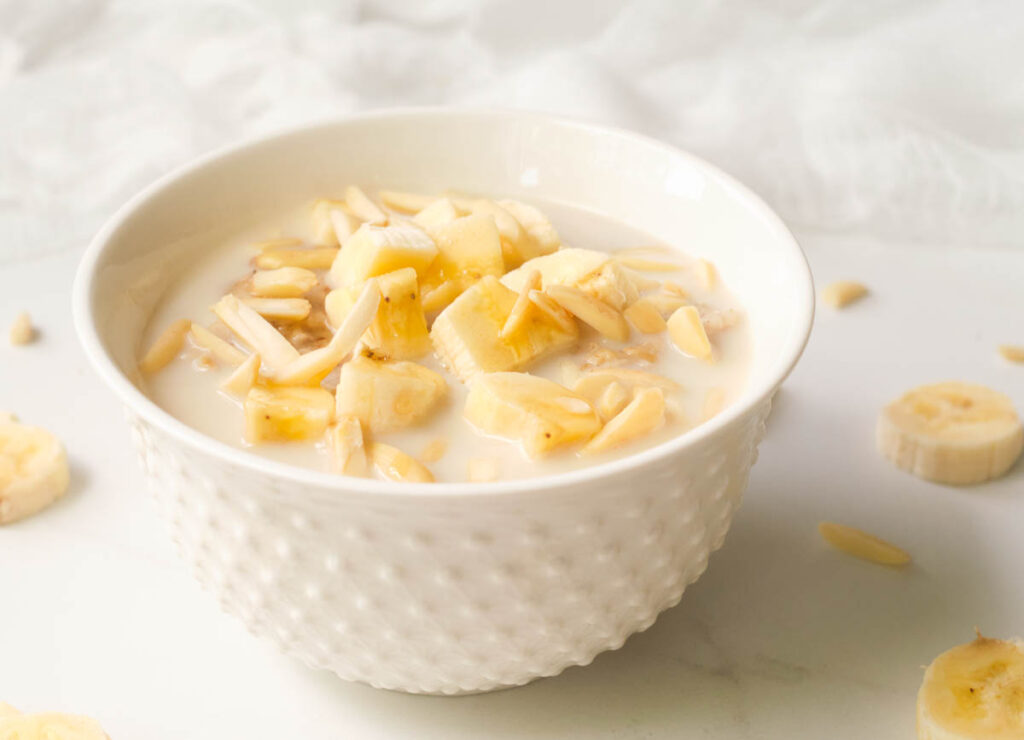 Bowl of oatmeal topped with almond milk, bananas, and almonds.