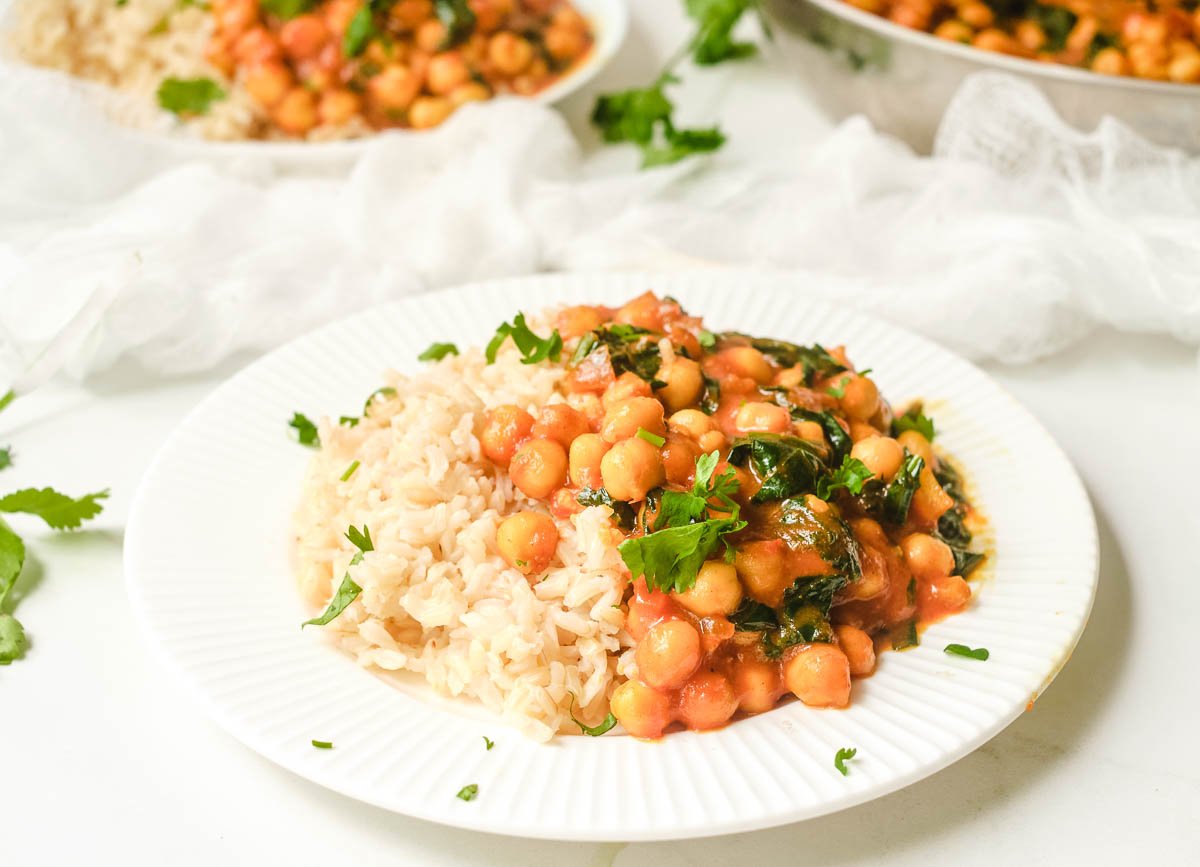 Chickpea curry spinach on white plate served with brown rice.