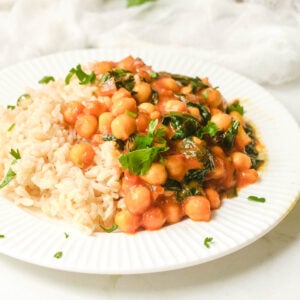 Chickpea curry spinach on white plate served with brown rice.
