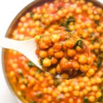 Spoon lifting chickpea spinach curry from pan.