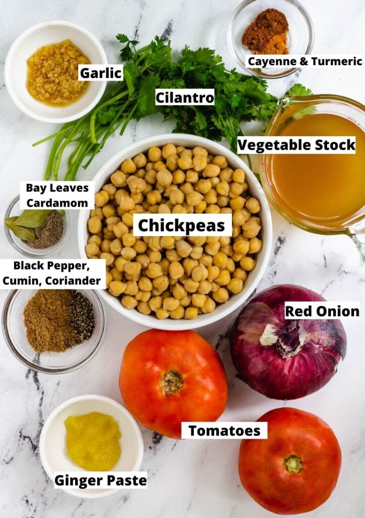 Ingredients for Punjabi Chole: minced garlic, cilantro, cayenne and turmeric, bay leaves, cardamom, chickpeas, vegetable stock, black pepper, cumin, coriander, red onion, tomatoes, and ginger paste.