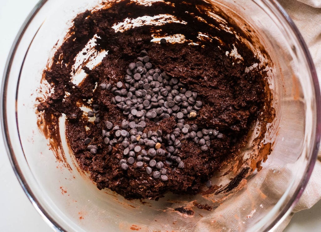 Chocolate chips added to brownie batter in glass bowl.