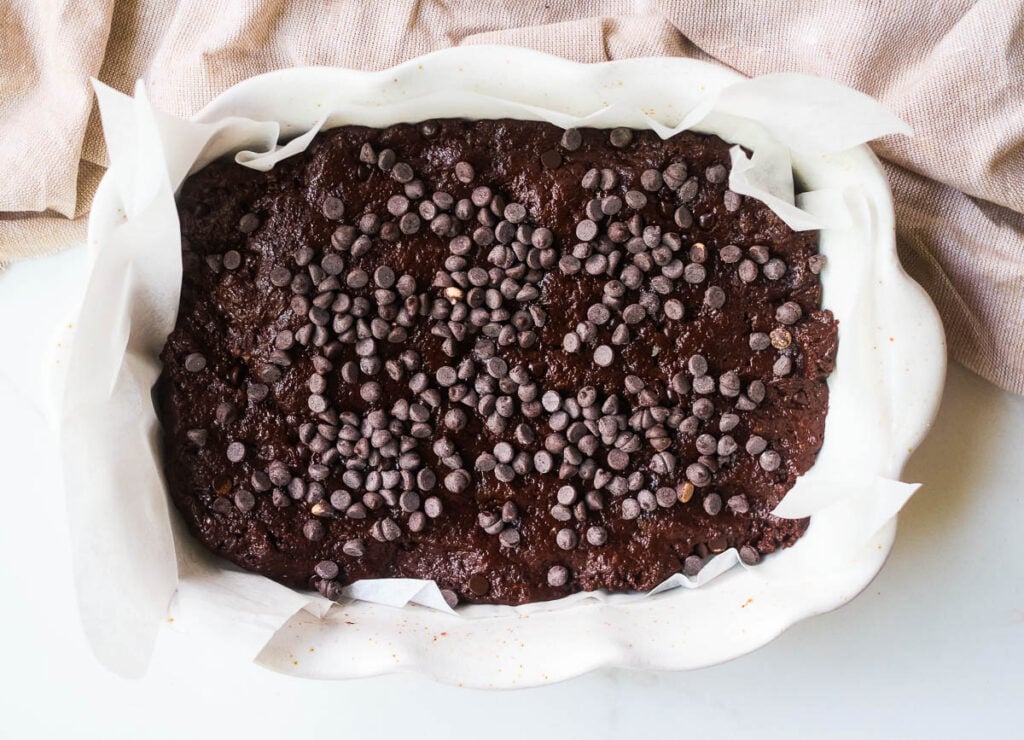 Brownie batter topped with chocolate chips in baking dish.