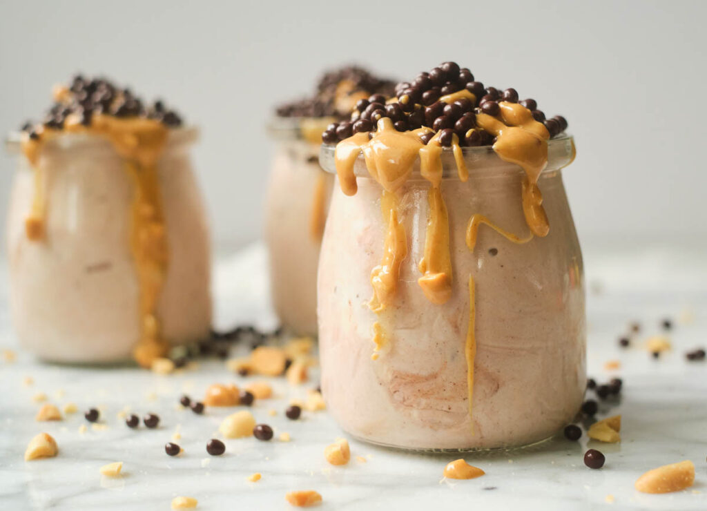 Yogurt in small glass jars topped with drizzle of peanut butter and chocolate covered quinoa.