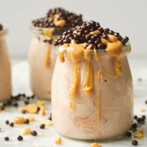 Peanut butter yogurt in small glass cup topped with drizzle of peanut butter and chocolate covered quinoa.
