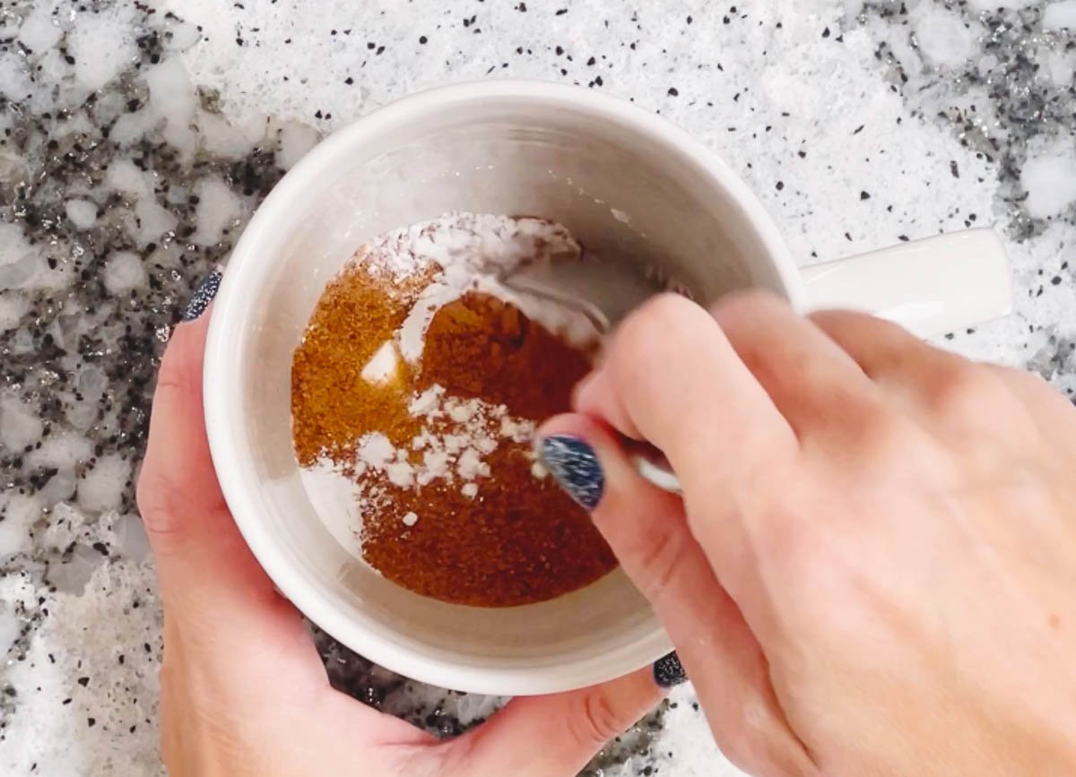 Mixing flour and pumpkin spice together in a mug.