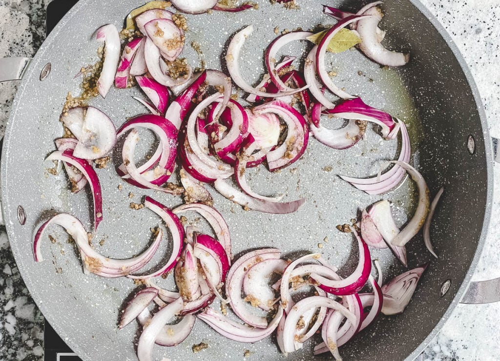 Thinly sliced red onion in pot with spices.