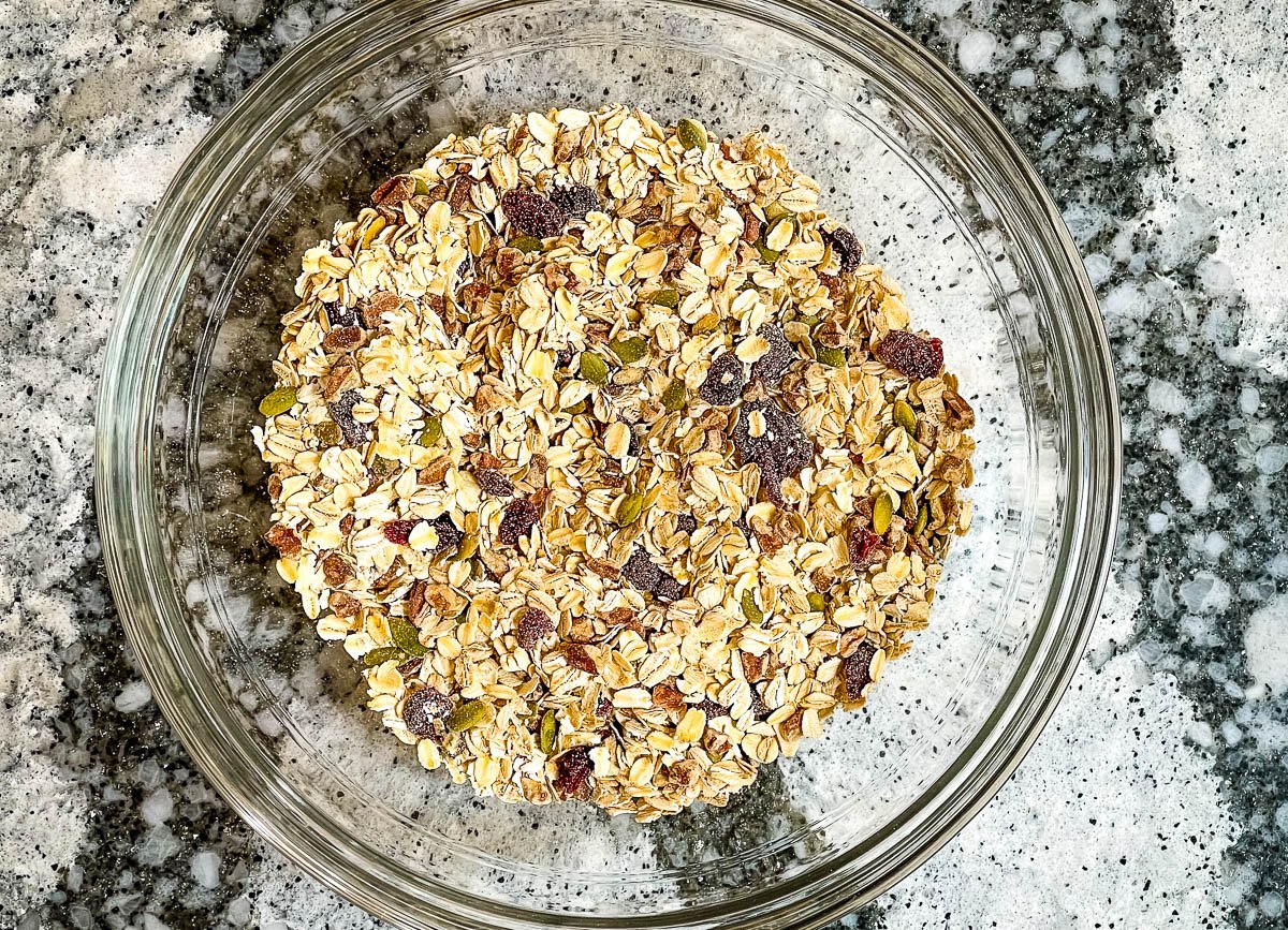 Oats, chia seeds, pumpkin seeds, and cranberries mixed together in a glass bowl.
