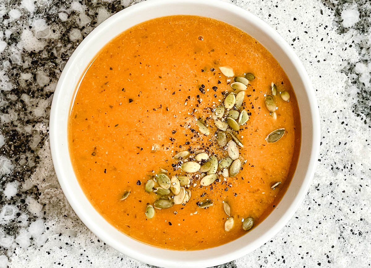 Pumpkin soup in bowl topped with pumpkin seeds and black pepper.