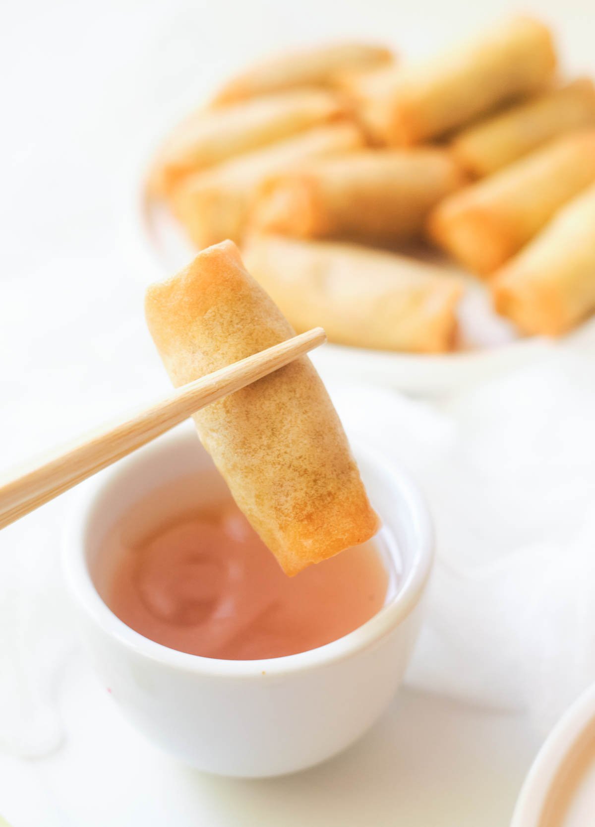 Spring roll held in chopsticks dipped in sweet and sour sauce. 