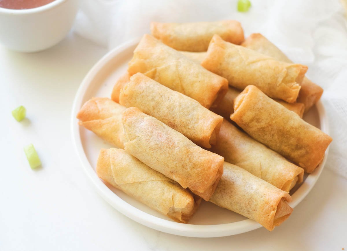 Cooked golden brown spring rolls on white plate. 