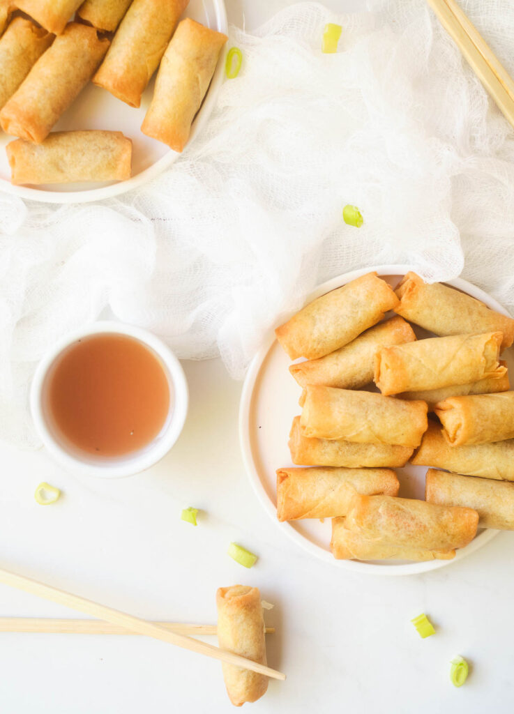 Frozen spring rolls on two white plates with a side of dipping sauce.